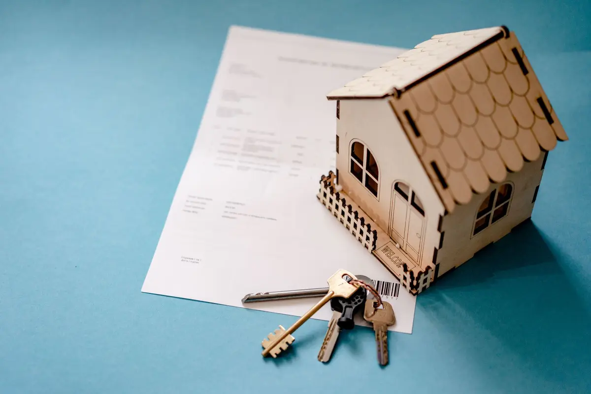 A set of house keys and a small wooden house model resting on a printed contract