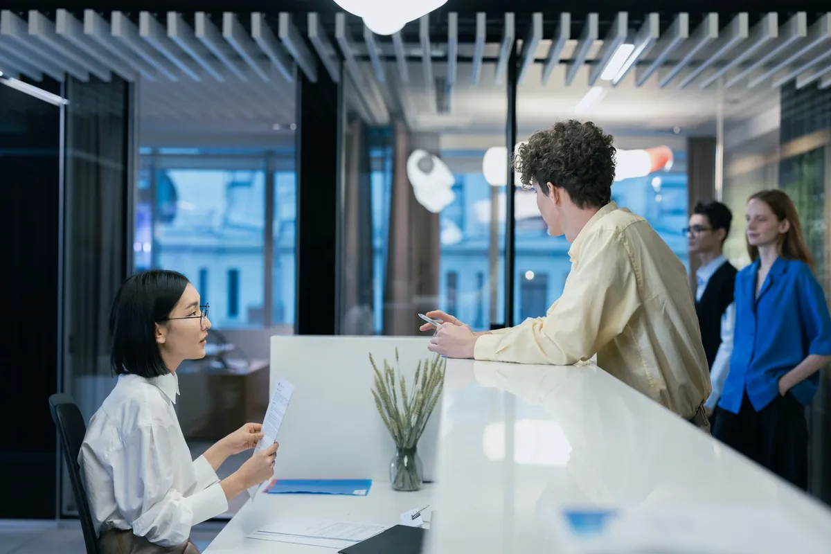 A member talking with a staff member across a bright service counter while others wait their turn