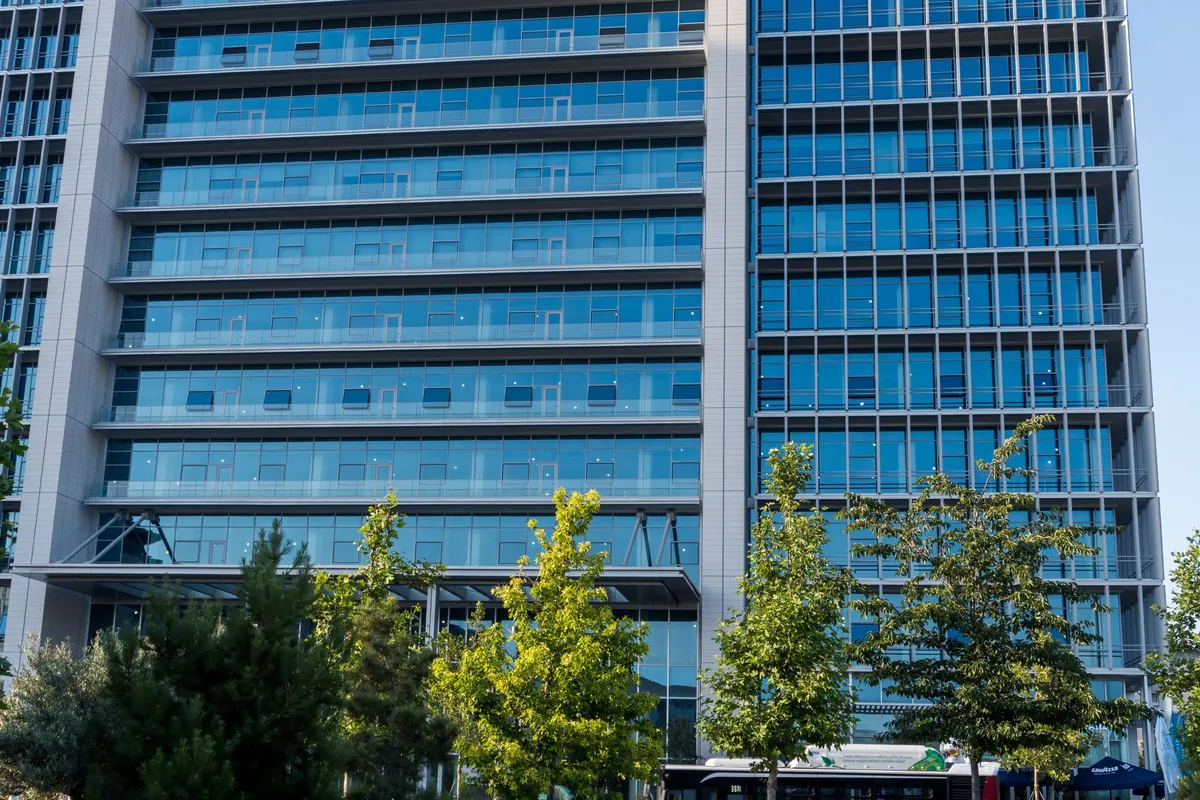 A glass-fronted commercial office building behind a row of young street trees