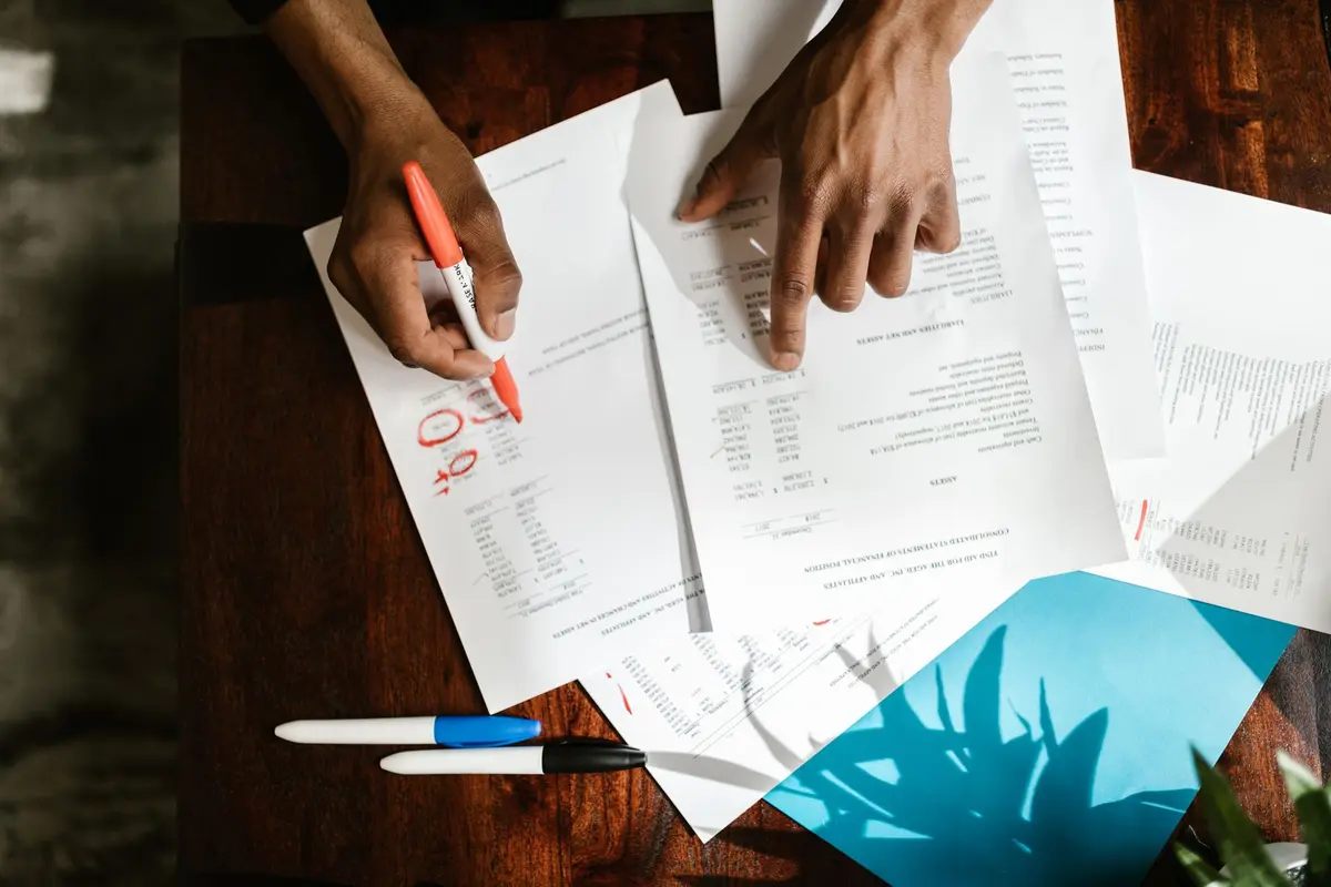 Hands marking up printed documents next to a laptop on a desk